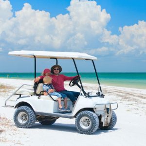 Man driving a golf cart on a beach with young kids as his passengers. 